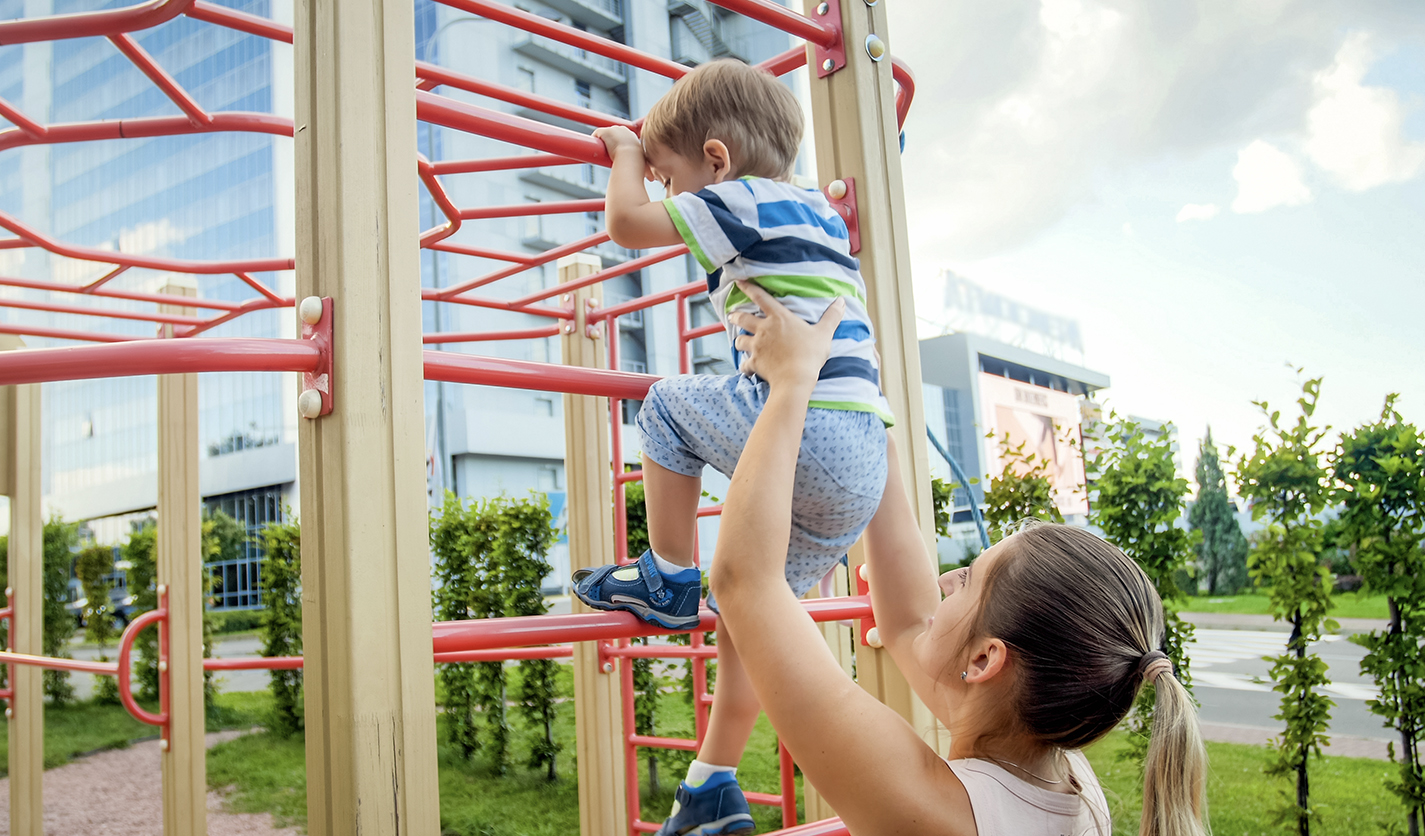 Mother helping younger son climb bars at the playground