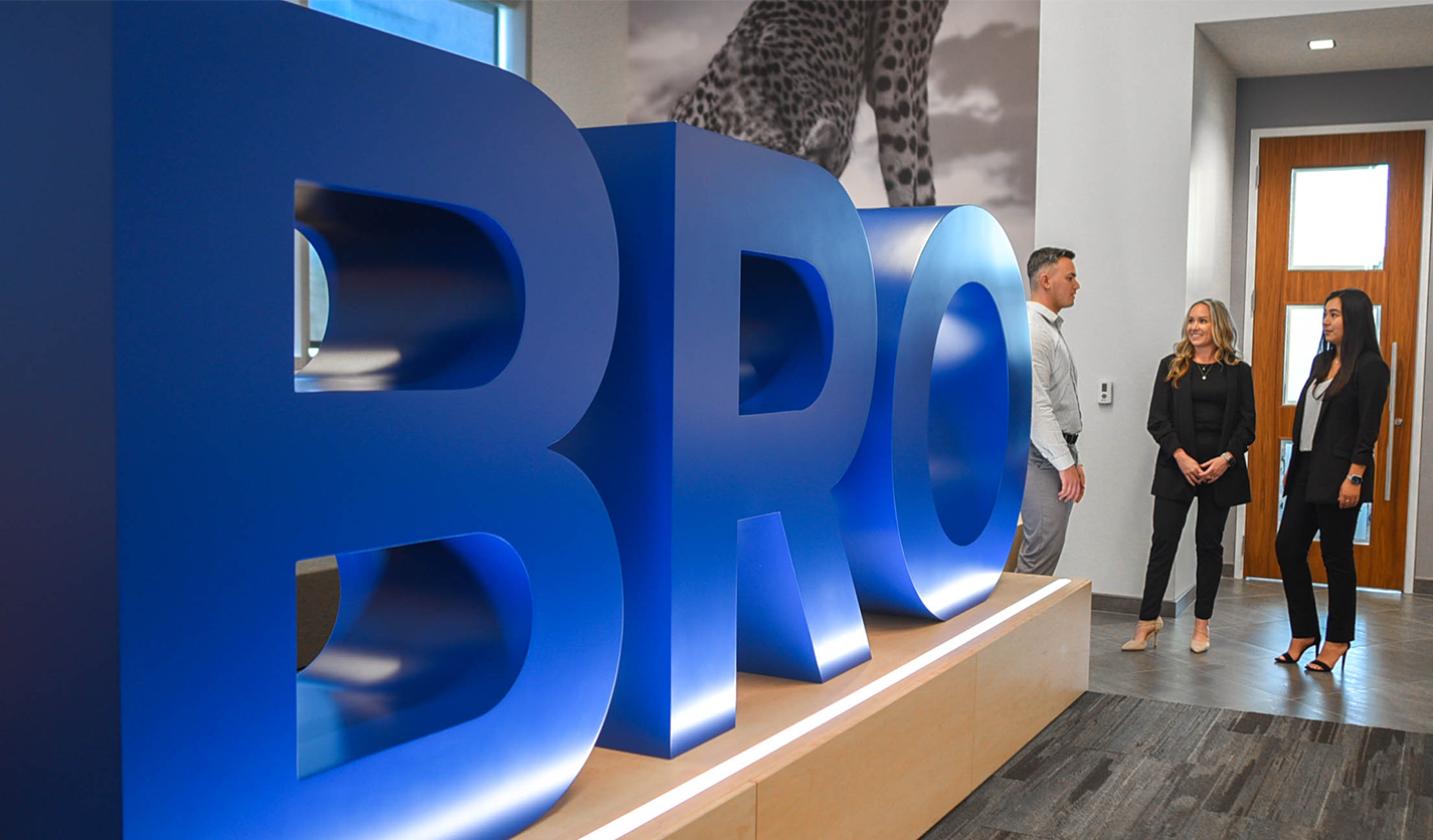 Three people standing together talking next to a large structure that says B-R-O in the campus headquarters.